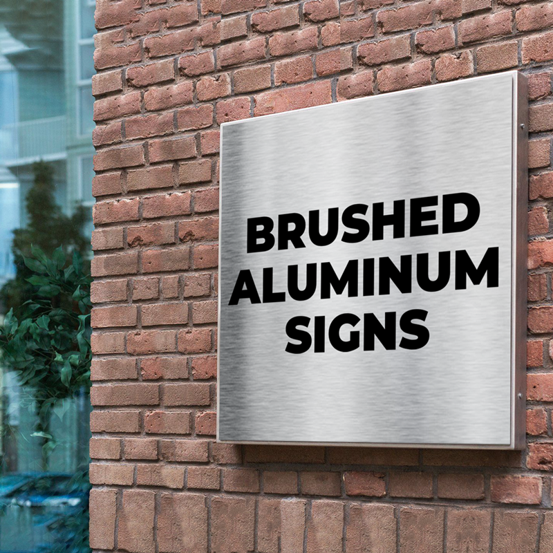 Brushed aluminum sign mounted on brick wall displaying bold black text 'Brushed Aluminum Signs